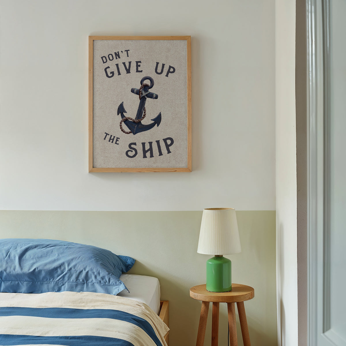 Room interior with a framed quote and anchor painting above a bed and a lamp on a side table.