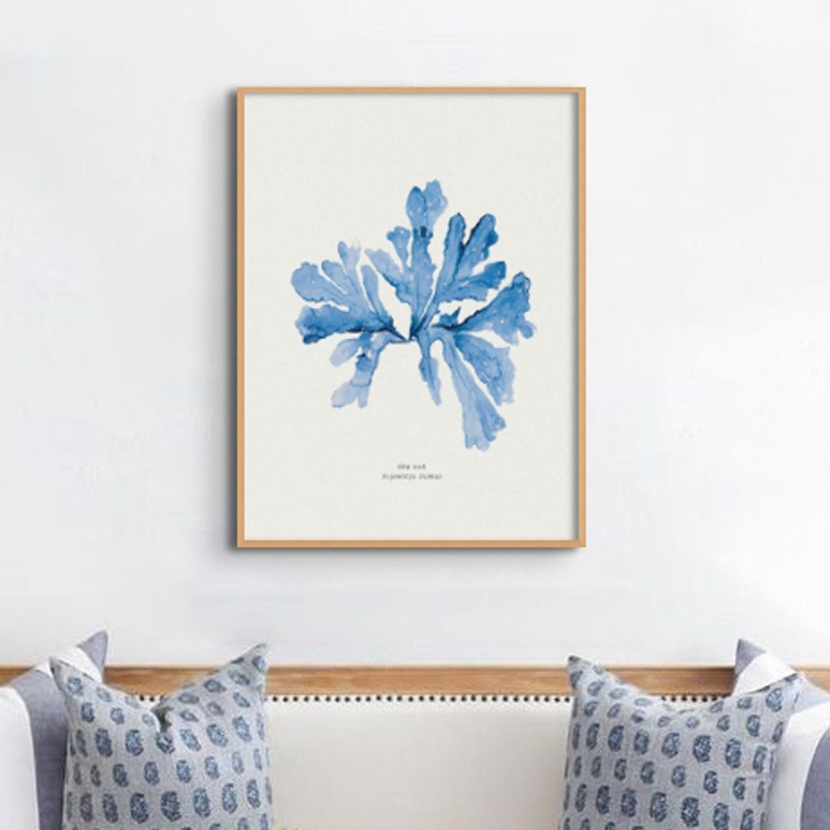 blue seaweed painting framed in a wooden frame on the wall above a sofa.