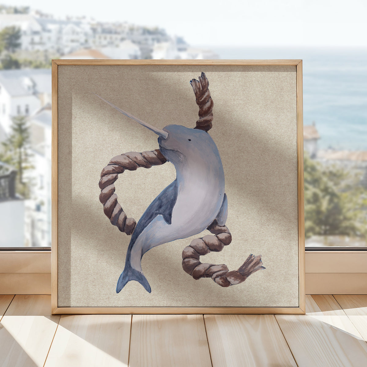 Framed artwork of a whale playing with a rope on a wooden floor with a window in the background.