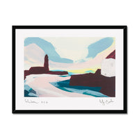 A framed abstract landscape art print featuring a stylized coastal scene with blue, pink and white foreground shapes, dark brown rock forms, and a pale sky. The print is mounted with a wide white mat and enclosed in a slim black frame, shown against a plain white background.