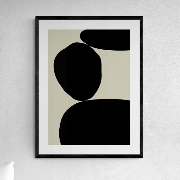 Framed abstract art print with black shapes on a beige background, hanging on a white wall.