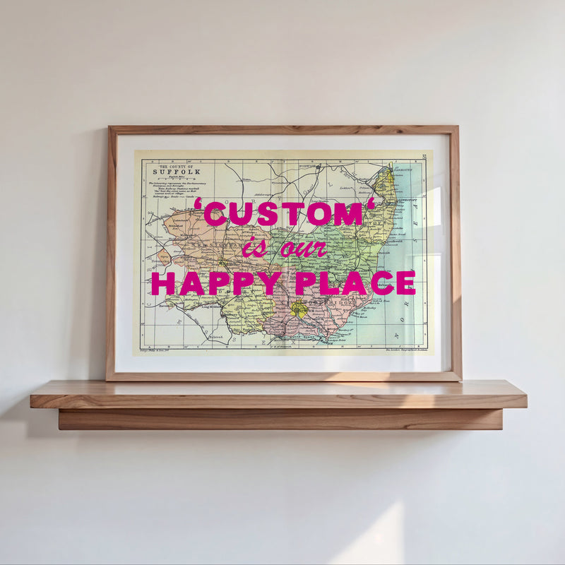 Framed map with 'Custom is our Happy Place' text on a wooden shelf against a white wall.
