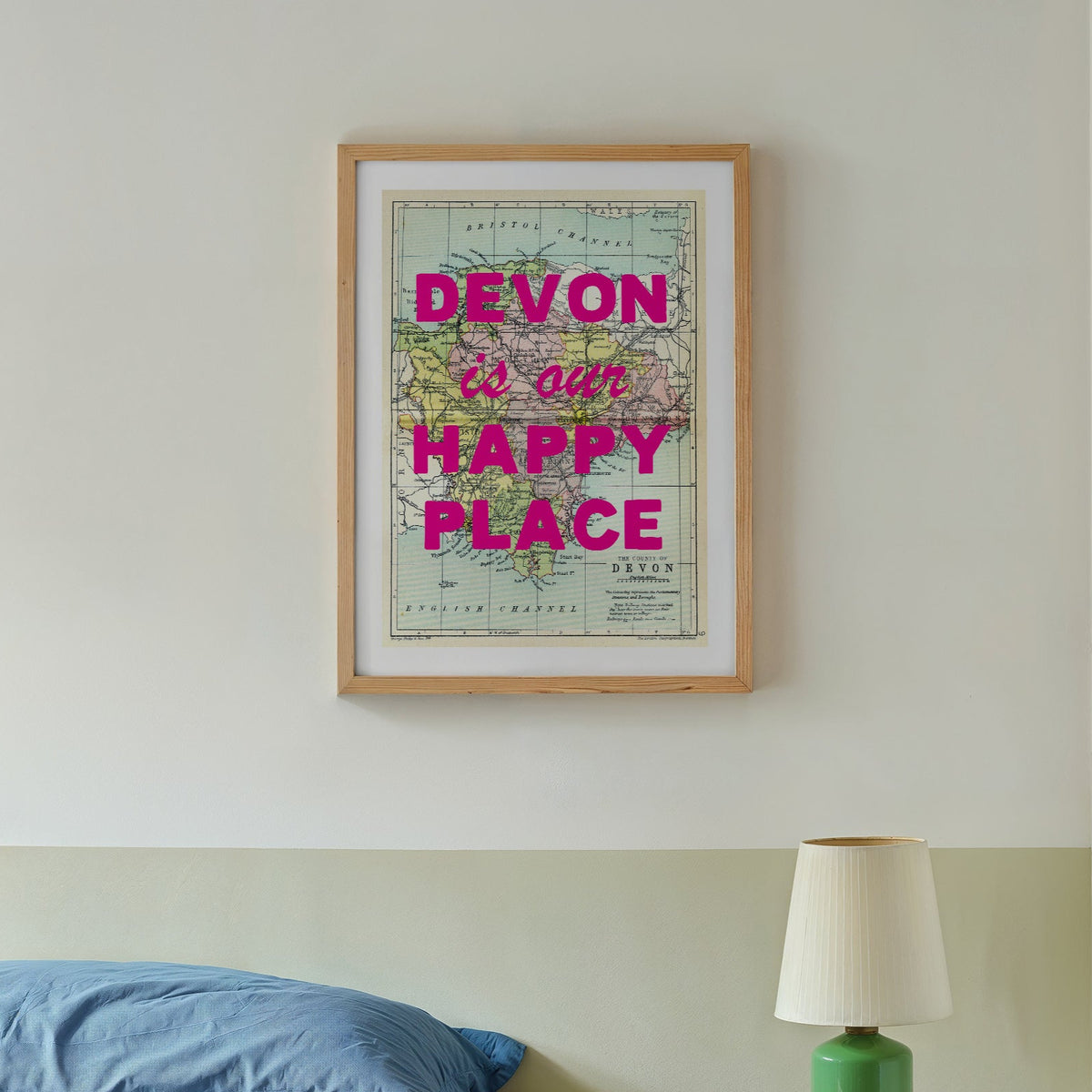 Bedroom with a framed map reading 'Devon is our happy place' above a bed.