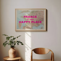 Framed map with 'France is our happy place' text on a wall above a plant and chair.