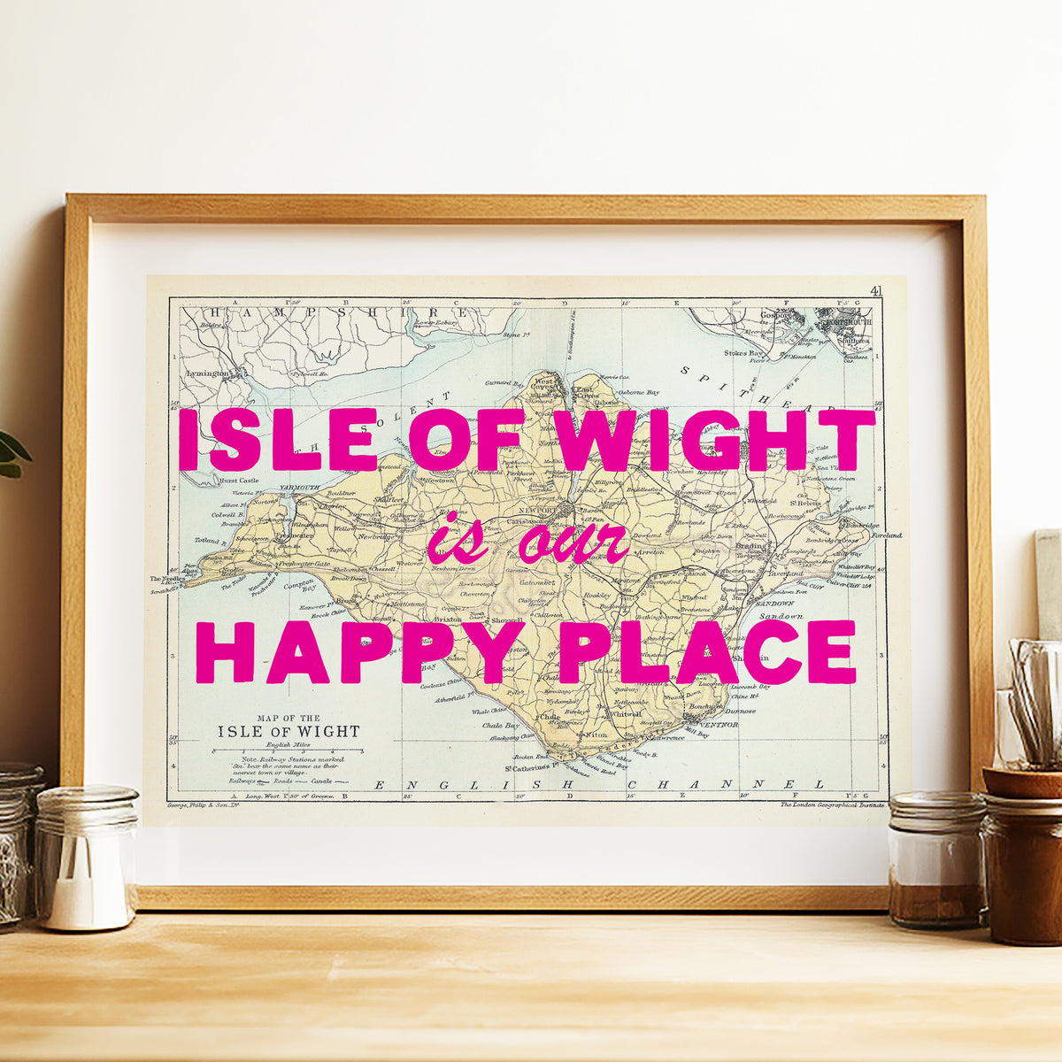 Framed map of the Isle of Wight with pink text on a wooden surface.