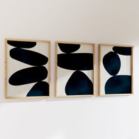 Three abstract art pieces with black shapes on a white wall