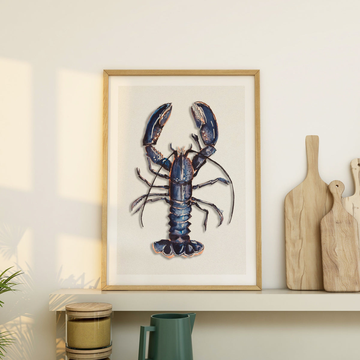 lobster print styled in a neutral kitchen interior on a shelf next to wooden chopping boards.