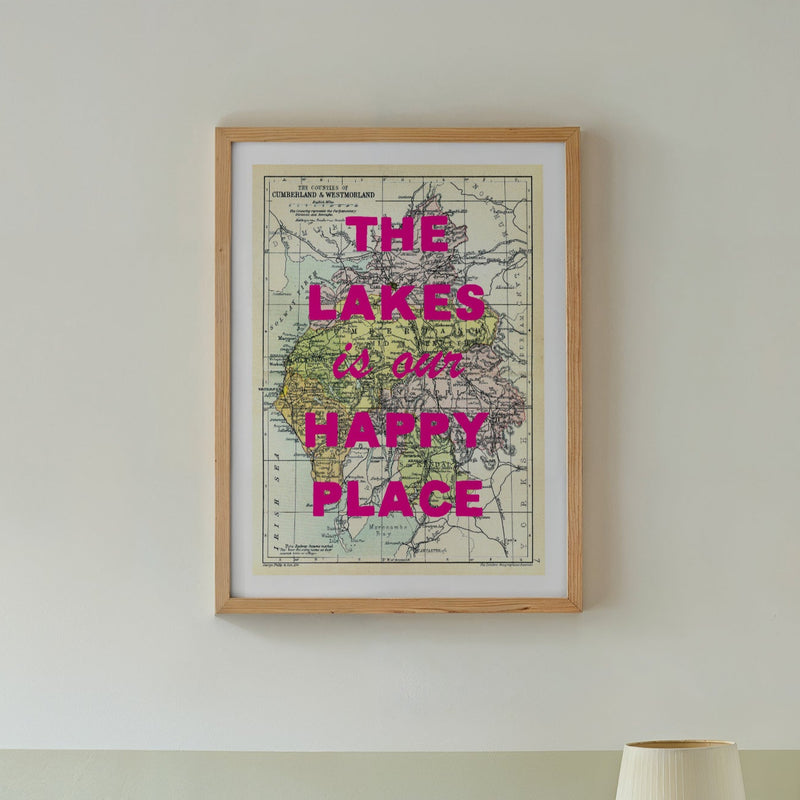 Framed map with 'The Lakes is our happy place' text above a bed in a bedroom.