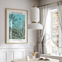 A framed coral art print in a dining room with a round table, chairs, and a window with curtains.