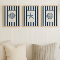 Three framed coastal-themed prints above a sofa with decorative pillows and a blanket.