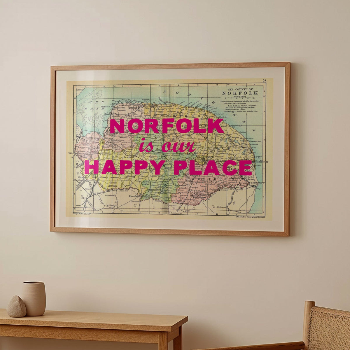 Framed map of Norfolk with 'Norfolk is our happy place' text in a room with a wooden table and chair.