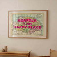 Framed map of Norfolk with 'Norfolk is our happy place' text in a room with a wooden table and chair.