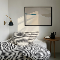 Modern bedroom with striped bedding, wall lamp, and abstract art.