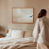 Person standing by a bed in a bedroom with abstract art on the wall.