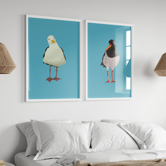Two framed artworks of birds on a wall above a sofa with lamps and books.