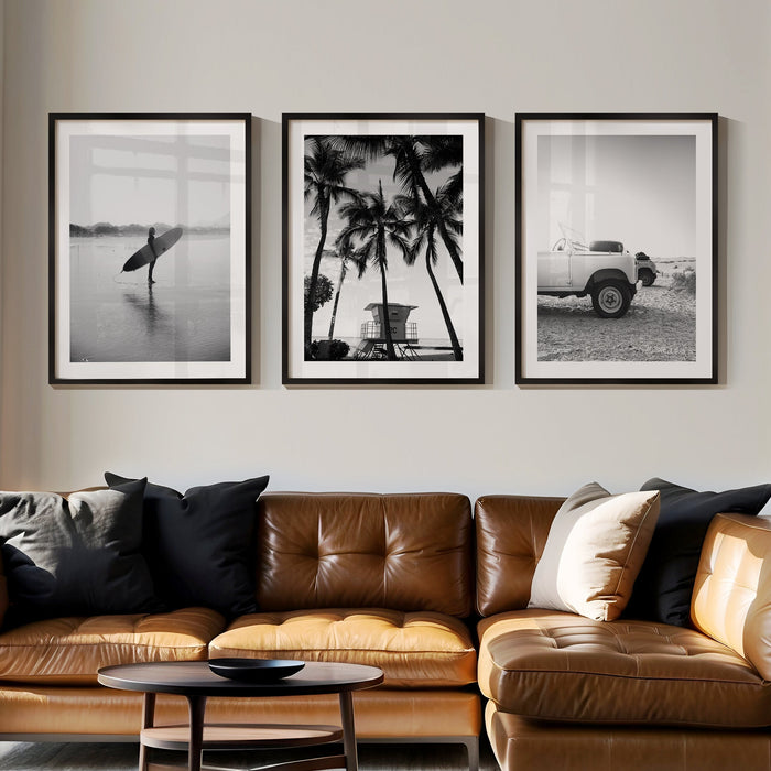 Set of three black and white beach photographs displayed above a sofa in a modern, featuring a palm tree, surf scene, and coastal Land Rover print.