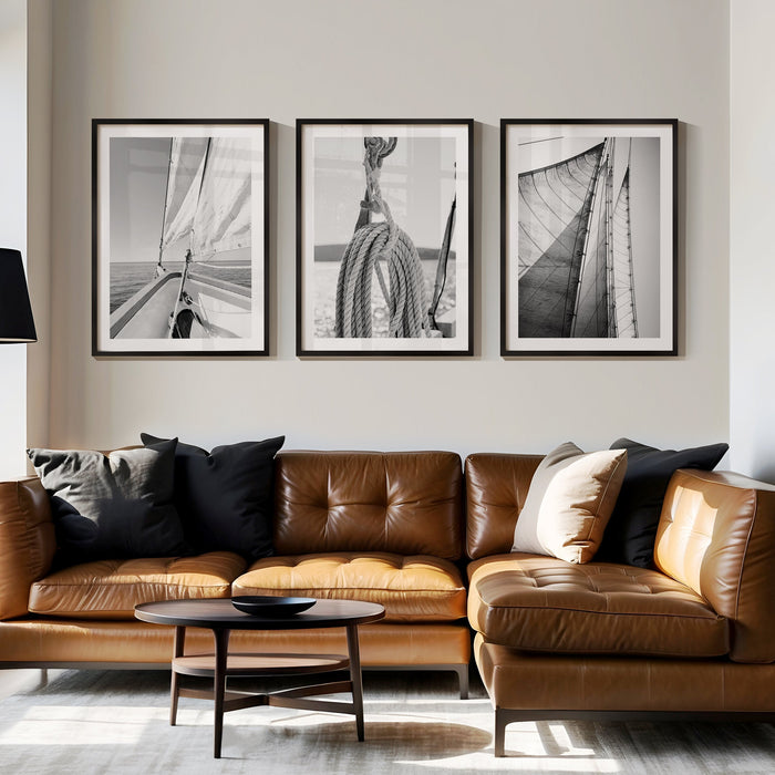 Set of 3 sailing themed art prints on wall above sofa. Modern living room with brown leather sofa, black coffee table, and framed black and white artworks on the wall.