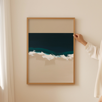 Person hanging a framed artwork of a beach scene on a wall.