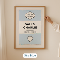 Personalised wedding/engagement print. Couple Print. Framed artwork with 'Sam & Charlie' text and heart symbol on a light blue background, held by a hand.