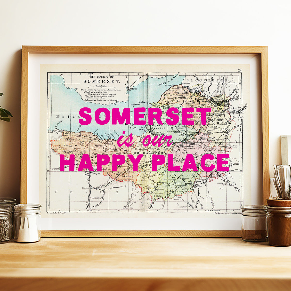Framed map of Somerset with 'Somerset is our happy place' text on a wooden surface.