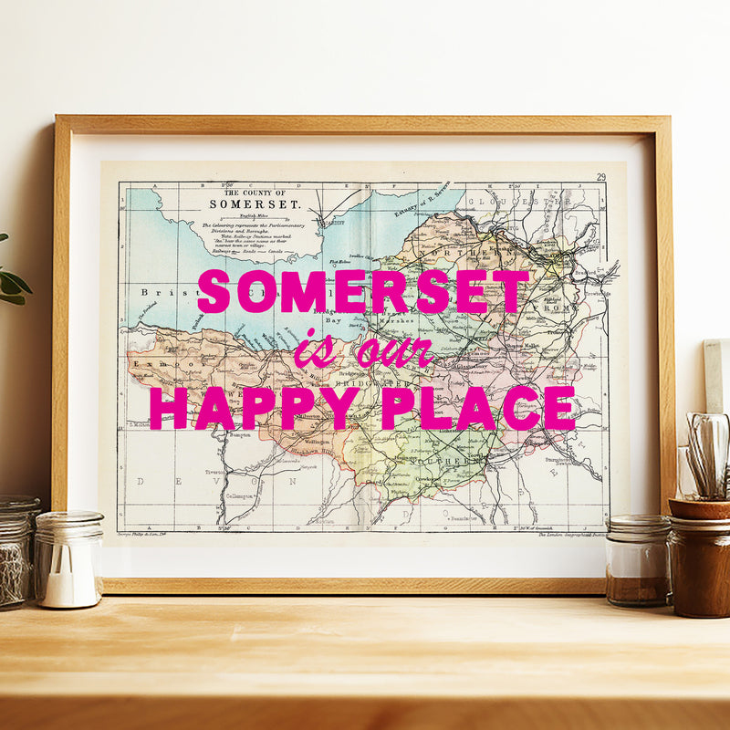 Framed map of Somerset with 'Somerset is our happy place' text on a wooden surface.