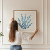 Watercolour seaweed print in blue, framed and being hung on wall