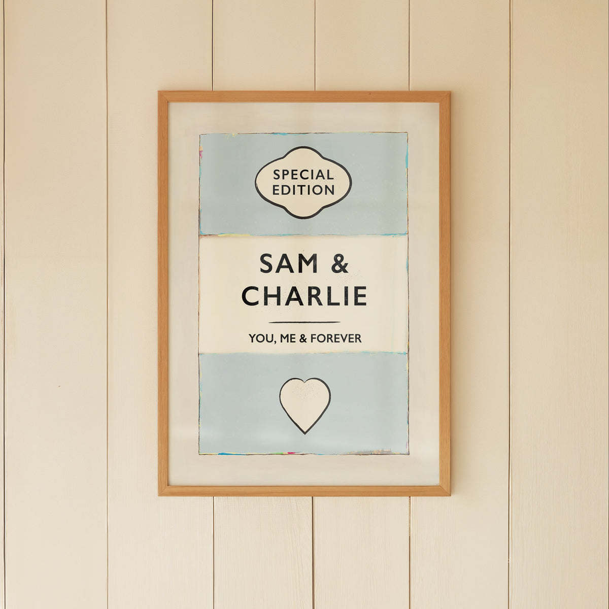 Framed artwork on a wall with a wicker chair and small table below.