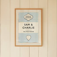 Framed artwork on a wall with a wicker chair and small table below.