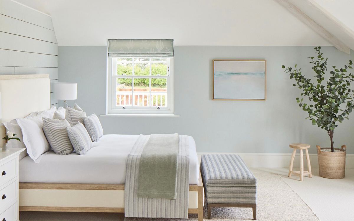 Modern sea painting in a bedroom with a bed, ottoman, and window view.
