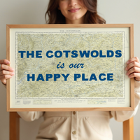 Person holding a framed map of the cotswolds with 'The Cotswolds is our happy place' text.