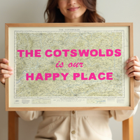 Person holding a framed cotswolds map with 'The Cotswolds is our happy place' text.