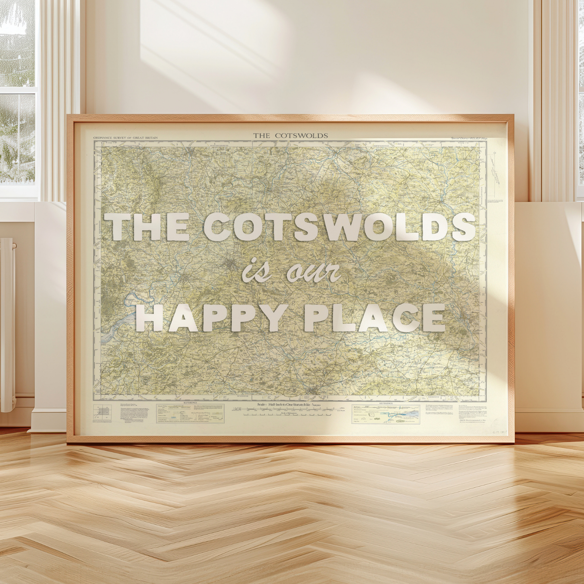 Framed map print of the Cotswolds with 'The Cotswolds is our happy place' text in a room with wooden floor and window.