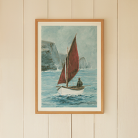 Framed artwork of a sailboat with a red sail on a beige wall.