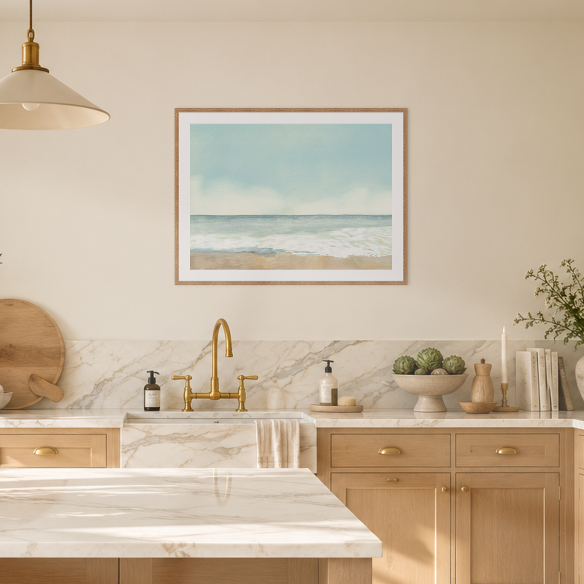 A framed art print depicting a calm ocean beach scene hangs on a beige wall above a marble sink and light wood kitchen cabinets.
