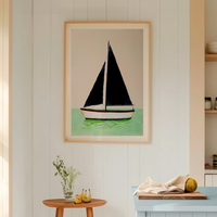 Framed artwork of a sailboat on a wall in a room with a table and plants.