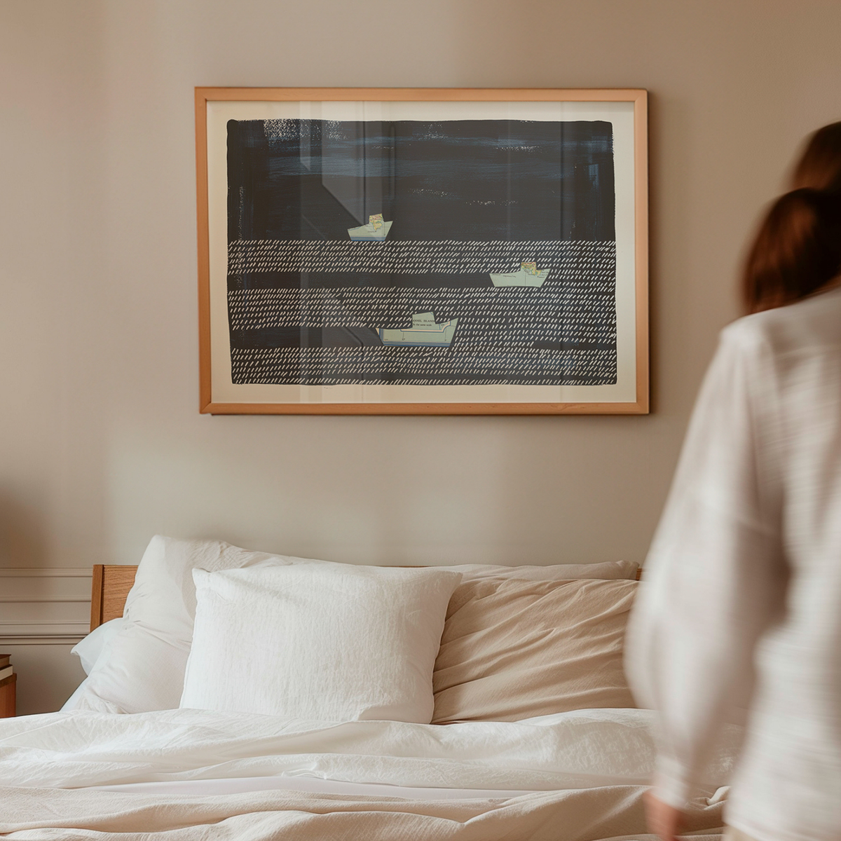 Framed fishing boat art print above bed in neutral bedroom with person walking by, navy coastal wall art