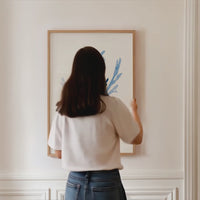 indigo seaweed print being hung on wall by lady - seaweed art print framed with natural wood frame on wall