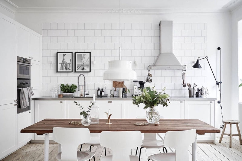 white family kitchen with farmhouse wooden table and wooden worktop. stainless steel cooker hood and white metro tiles. black and white sail photos above kitchen sink