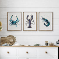 set of three shellfish prints in a white kitchen above a worksurface. Lobster print, crab painting and prawn painting.