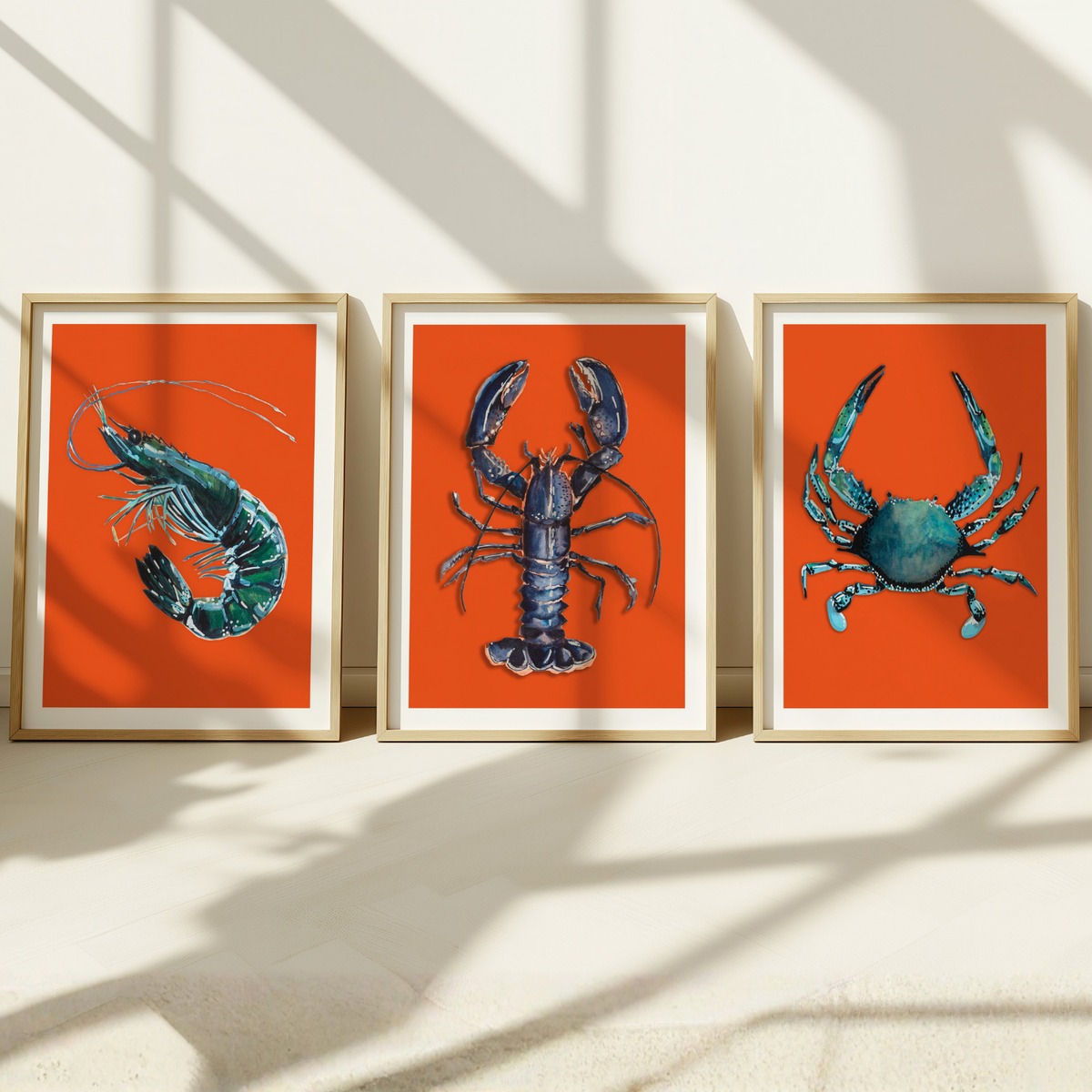 Set of three shellfish art prints - colourful kitchen at of three framed artworks of a prawn, lobster, and crab on orange backgrounds.