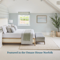 Modern bedroom with a bed, bench, and window view of greenery with minimalist sea painting on wall.