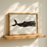 Framed artwork of a whale on a wooden shelf with sunlight casting shadows.