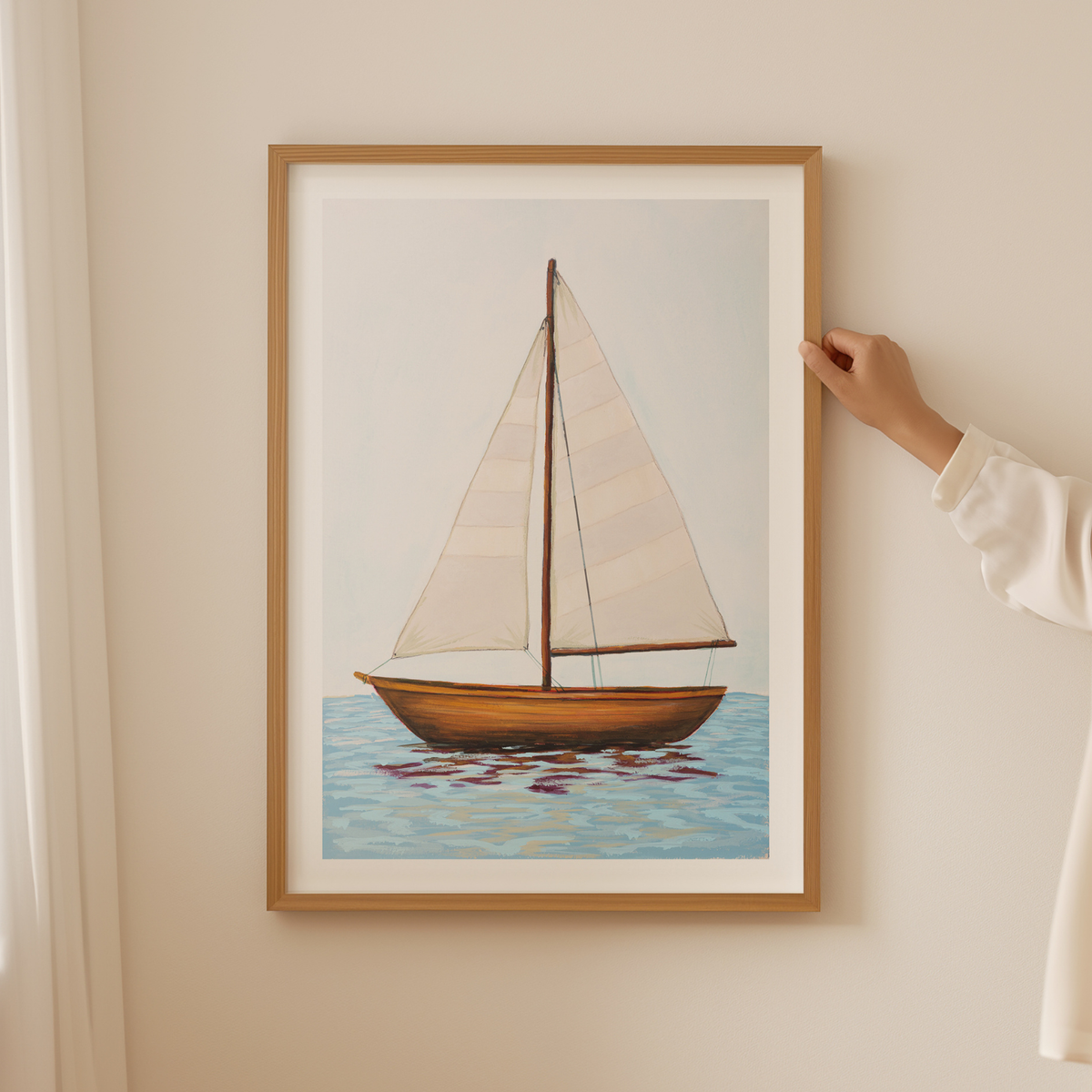 Framed artwork of a sailboat on a wall with a hand adjusting the frame.