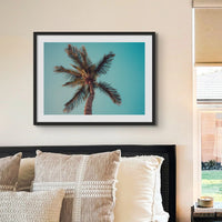 coloured beach art photograph of a palm tree against a blue green sky in a black frame in a neutral coastal bedroom- beach house art