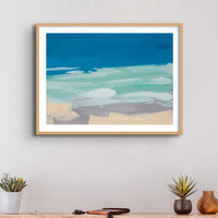 Watercolour coastal painting in blue and sand above a side table - Framed in a black frame