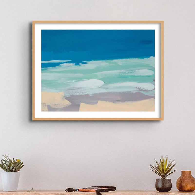 Watercolour coastal painting in blue and sand above a side table - Framed in a black frame