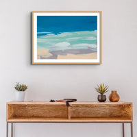 Watercolour coastal painting in blue and sand above a side table - Framed in a black frame