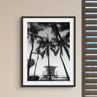 black & white beach art photograph of a life savers cabin in a palm tree grove in a black frame in a kitchen with shutters - beach house art