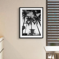 black & white beach art photograph of a life savers cabin in a palm tree grove in a black frame in a kitchen with shutters - beach house art