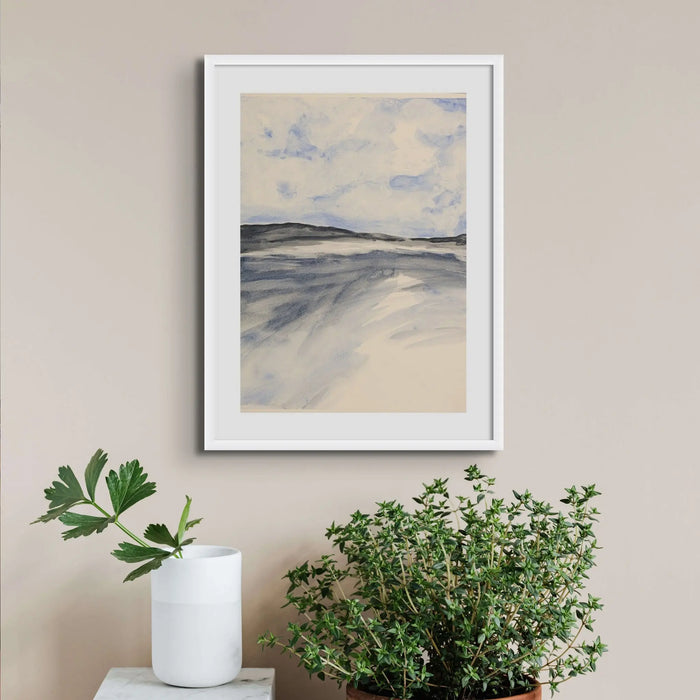 A framed watercolour painting of a coastal beach scene with low tide exposure. Framed on wall above potted plants.
